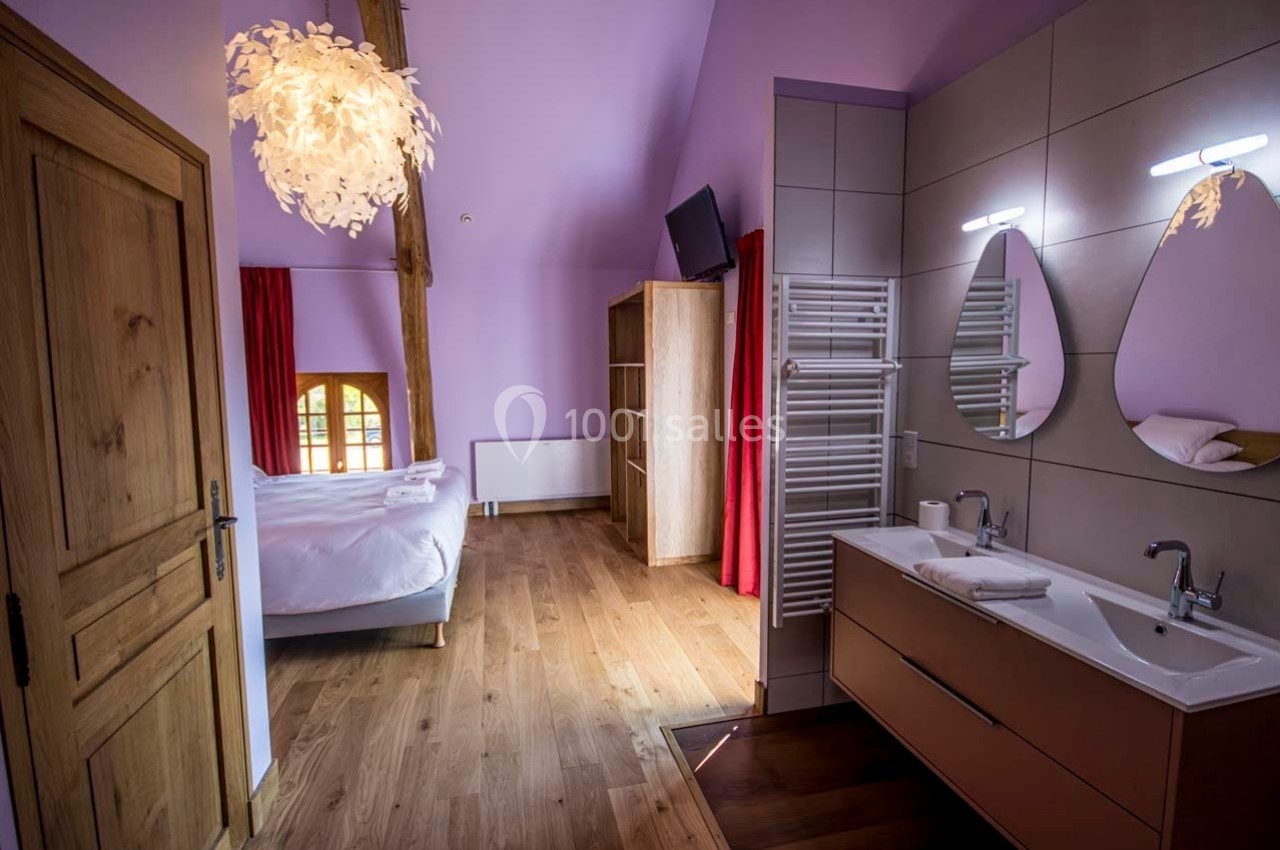 Chambre lumineuse avec lit double, parquet, salle de bain attenante avec double vasque et décoration moderne.
