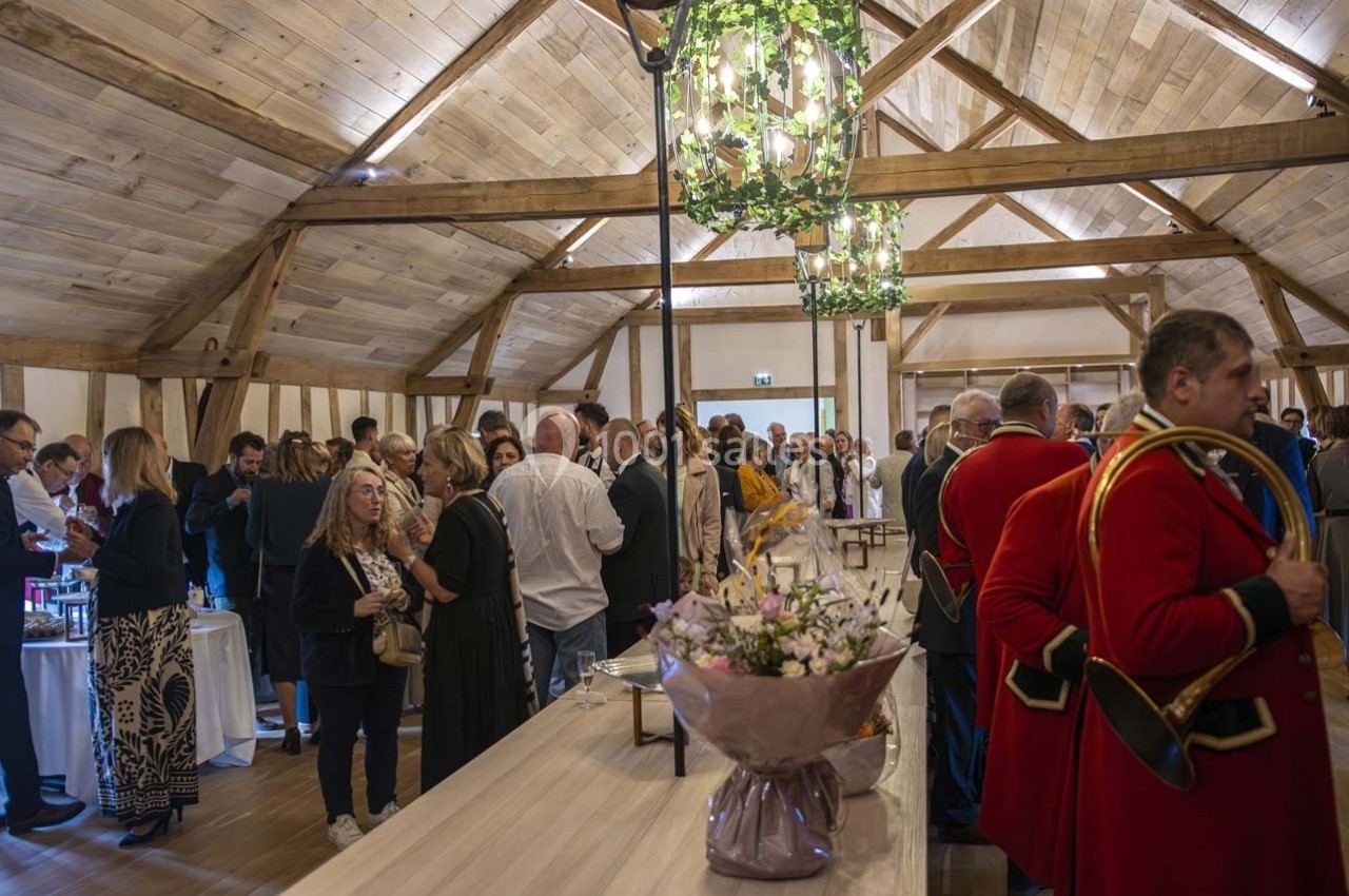 Salle en bois avec des invités debout lors d'un événement, décorée de lustres et d'un bouquet de fleurs au premier plan.