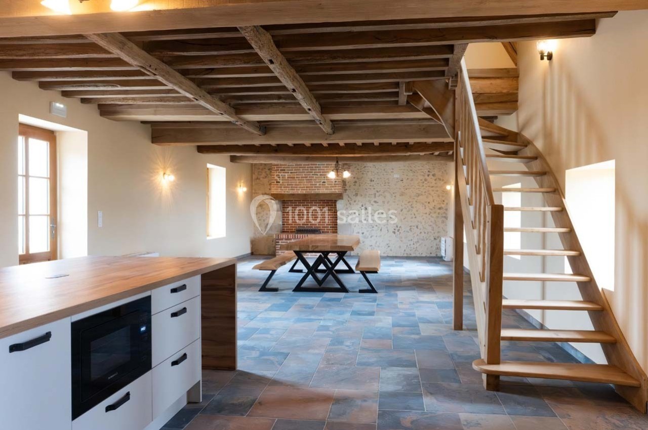 Cuisine ouverte avec îlot central en bois, escalier en colimaçon, murs en pierre et poutres apparentes dans un intérieur…