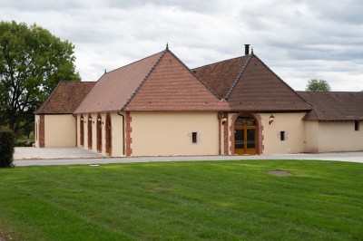 Chambre avec lit double, poutres apparentes, linge de lit blanc, et salle de bain attenante visible par une porte ouverte.