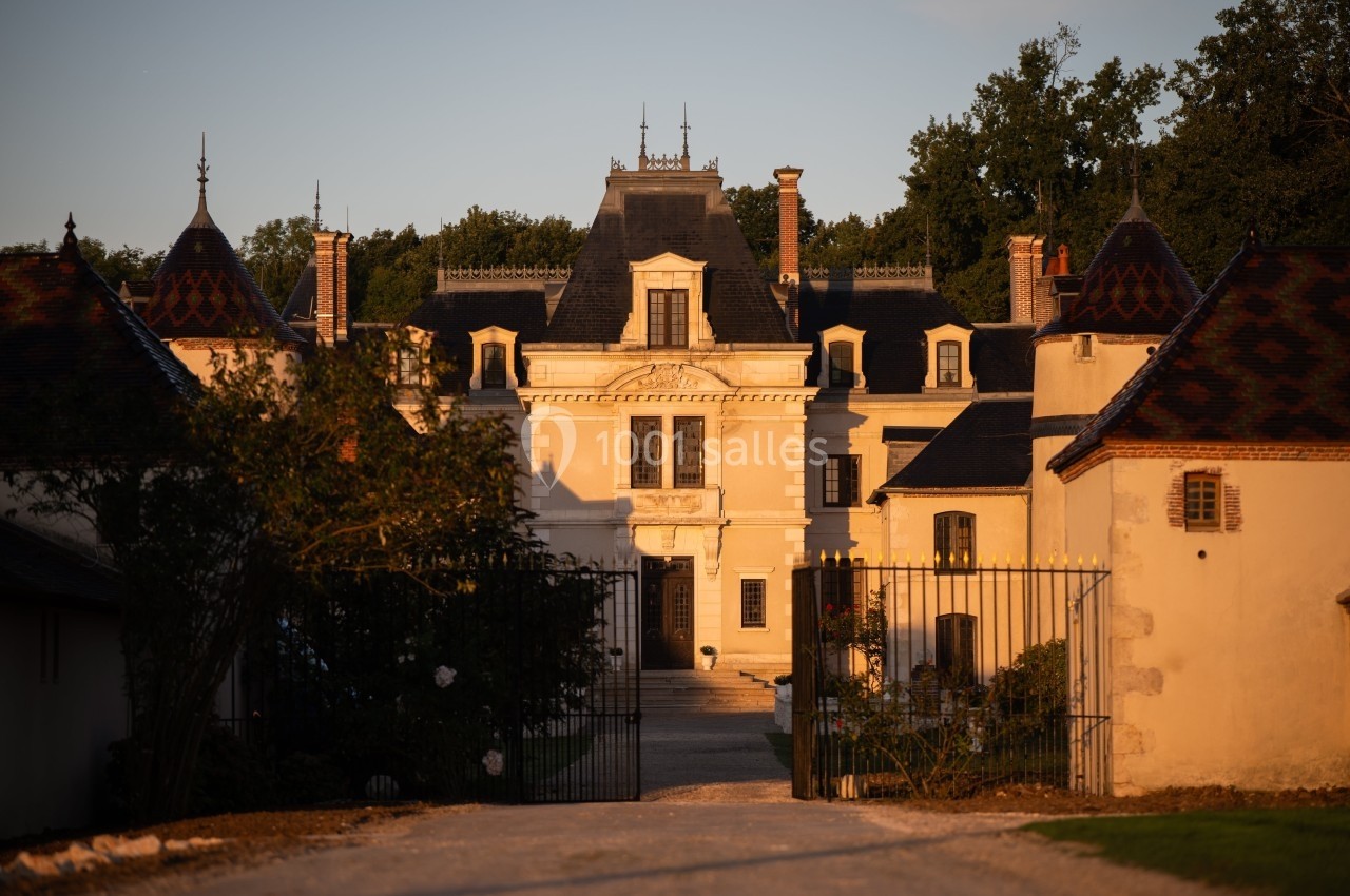 Façade d'un château historique entouré de dépendances, éclairé par une lumière dorée au coucher du soleil.