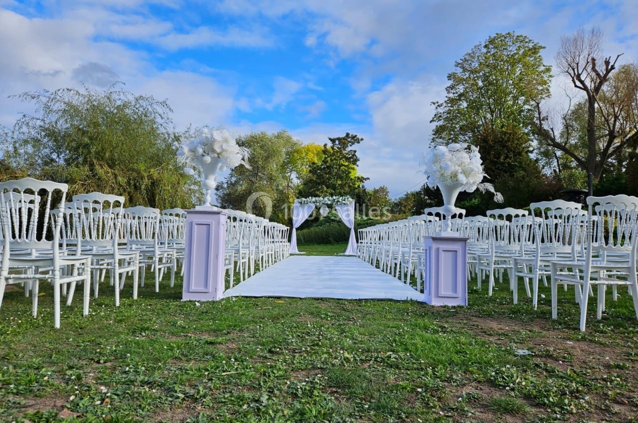 Allée centrale bordée de chaises blanches menant à une arche décorée pour une cérémonie en plein air.