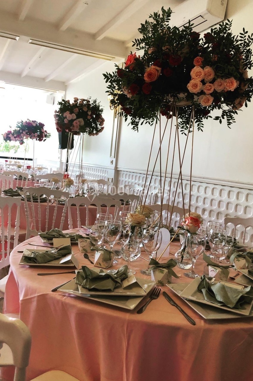 Salle de réception décorée avec des tables rondes nappées de rose, ornées de centres de table fleuris et élégants.
