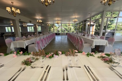 Buffet décoré avec des ballons roses et blancs, plats variés, et un cochon rôti sur une table drapée de blanc.