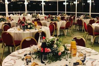 Buffet décoré avec des ballons roses et blancs, plats variés, et un cochon rôti sur une table drapée de blanc.