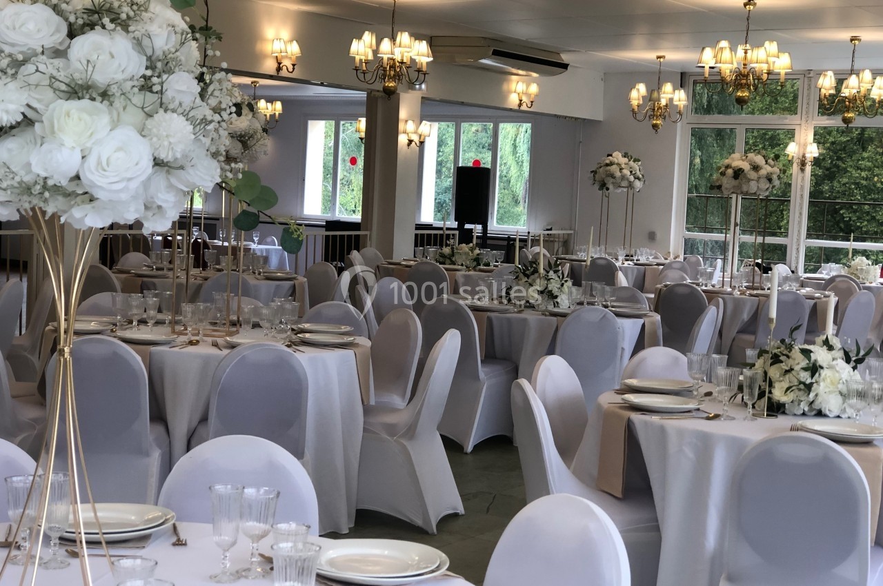Salle de réception élégante décorée de nappes blanches, fleurs blanches et lustres suspendus.