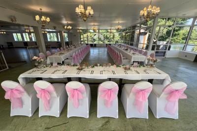 Buffet décoré avec des ballons roses et blancs, plats variés, et un cochon rôti sur une table drapée de blanc.