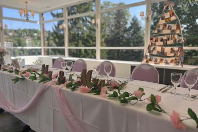 Buffet décoré avec des ballons roses et blancs, plats variés, et un cochon rôti sur une table drapée de blanc.