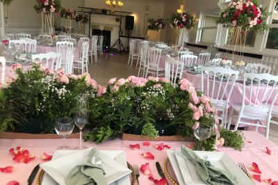 Buffet décoré avec des ballons roses et blancs, plats variés, et un cochon rôti sur une table drapée de blanc.