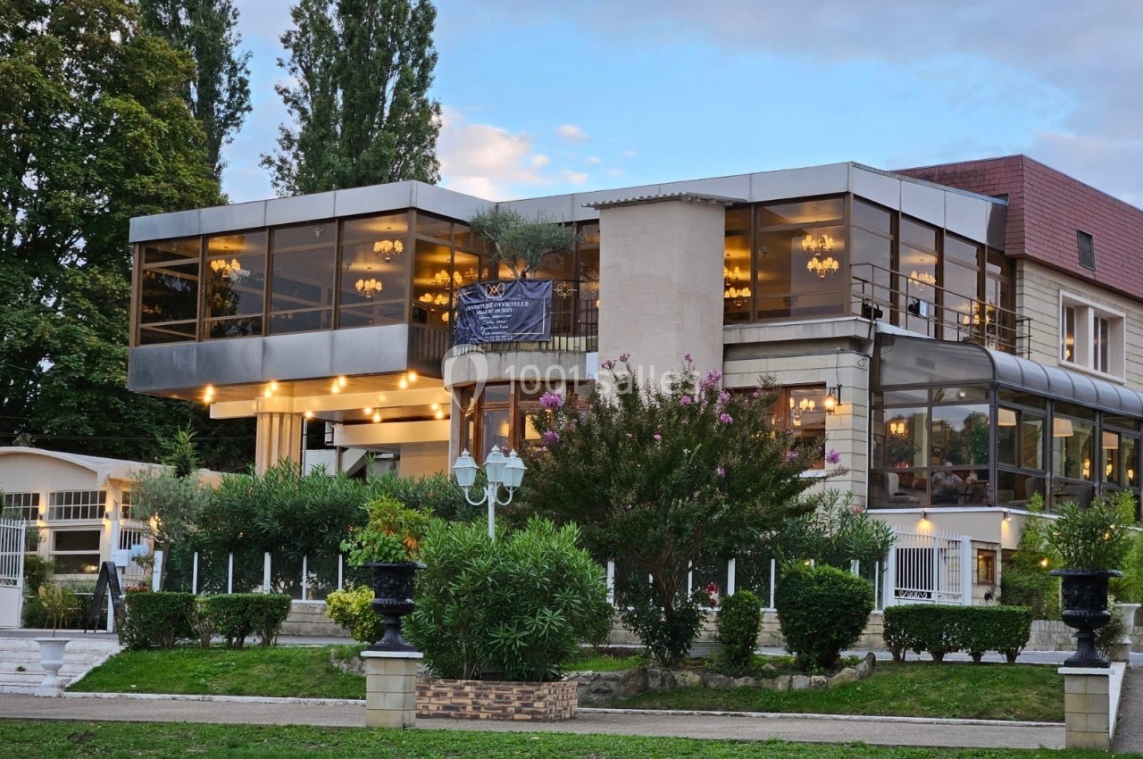 Bâtiment moderne avec grandes baies vitrées, entouré de verdure et éclairé par des lumières chaudes en soirée.