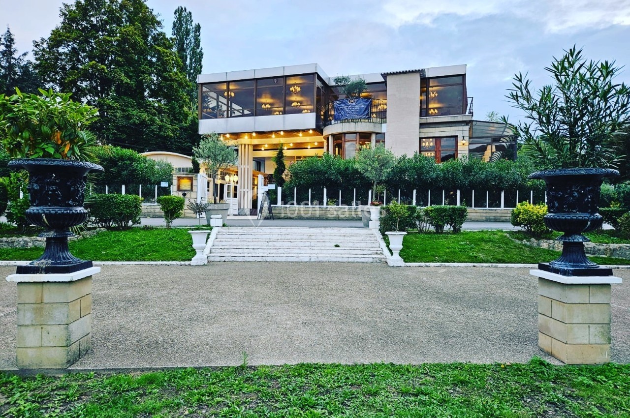 Façade d'un bâtiment moderne entouré de verdure, avec des escaliers menant à l'entrée principale éclairée.