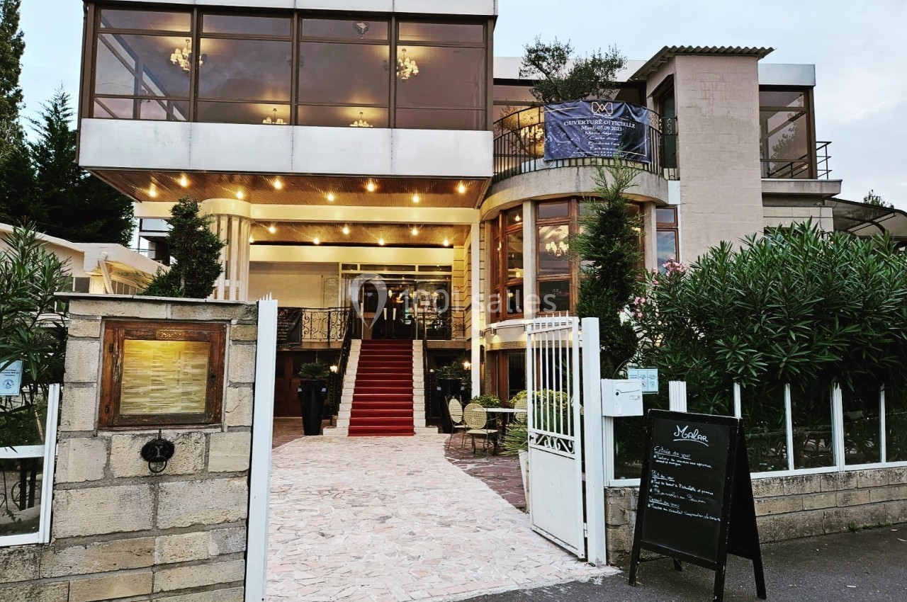 Façade d'un restaurant avec une entrée surmontée de grandes baies vitrées et un tapis rouge menant à la porte principale.