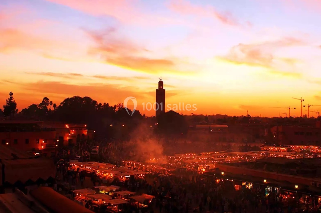 Place animée au coucher du soleil avec une mosquée en arrière-plan et des étals illuminés au premier plan.