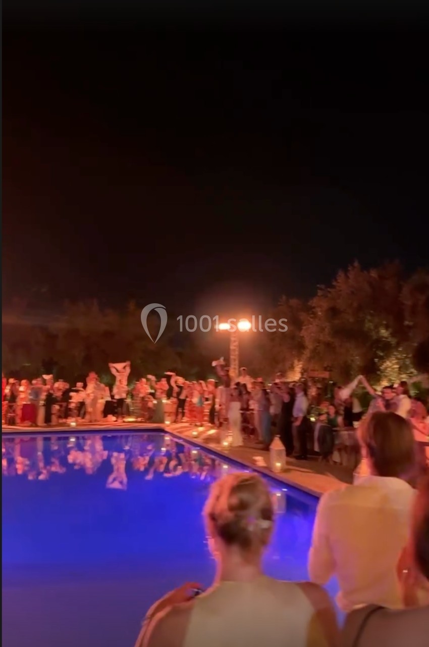 Des personnes rassemblées autour d'une piscine éclairée la nuit, certaines brandissant des objets lumineux.