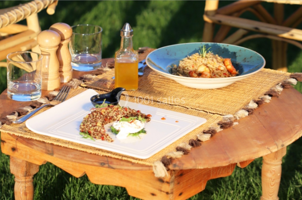 Table basse en bois sur pelouse, dressée avec plats de céréales, assaisonnements, verres et accessoires de service.