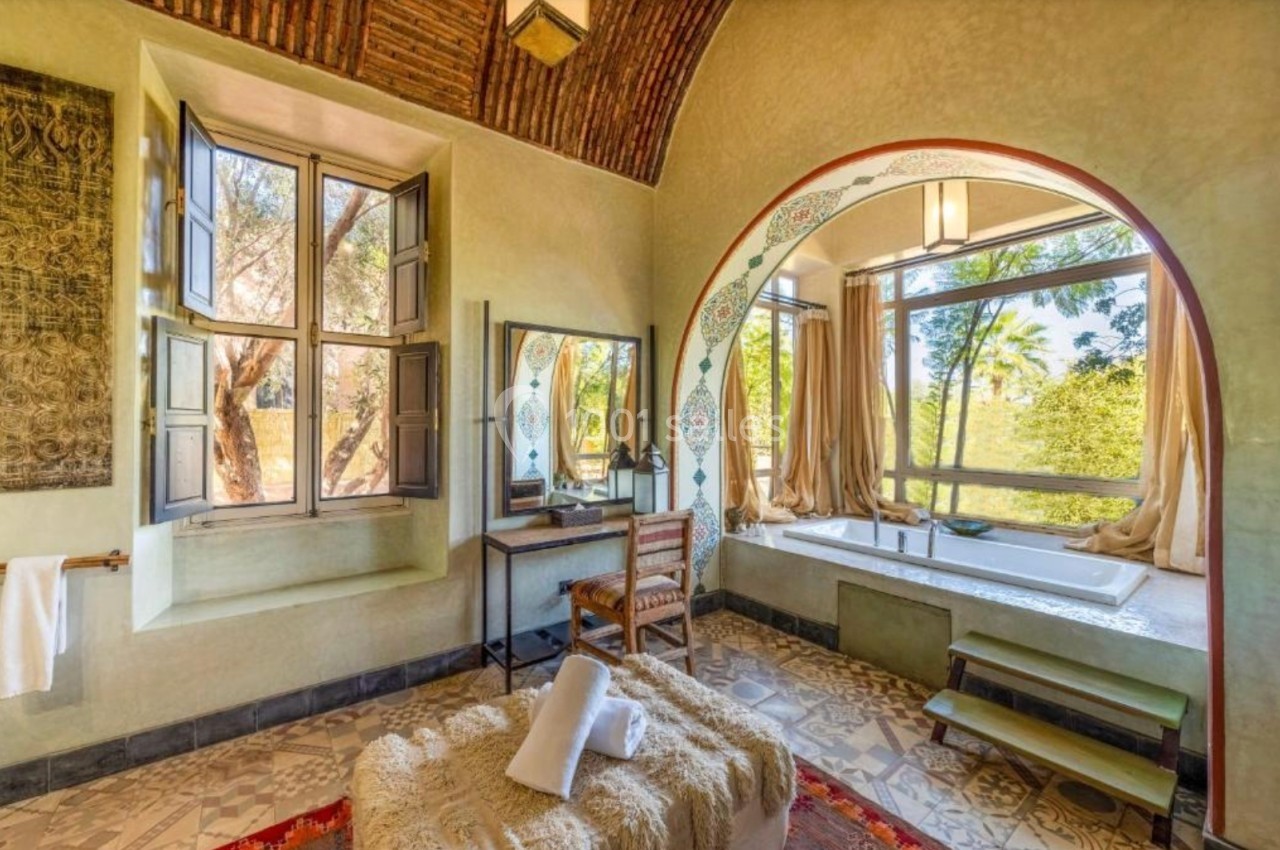 Salle de bain lumineuse avec baignoire près d'une grande fenêtre, murs décorés et plafond voûté en briques.