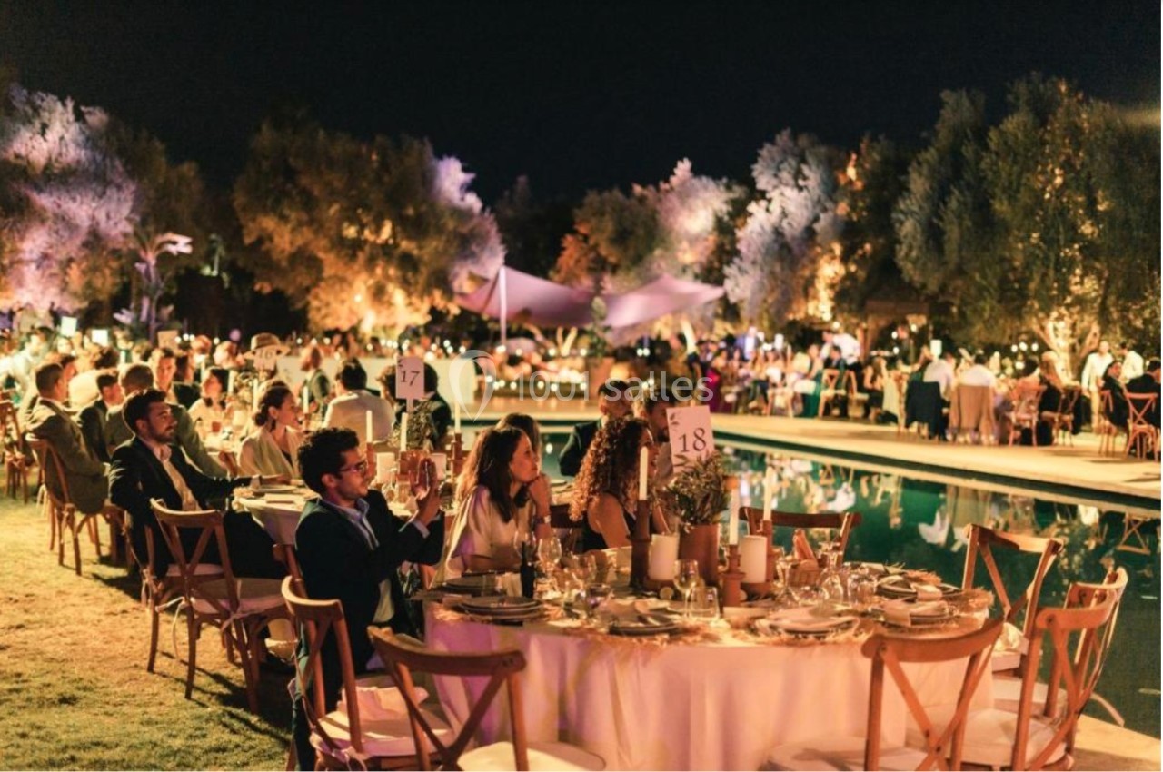 Des invités assis à des tables décorées près d'une piscine, lors d'un événement en soirée éclairé par des lumières.