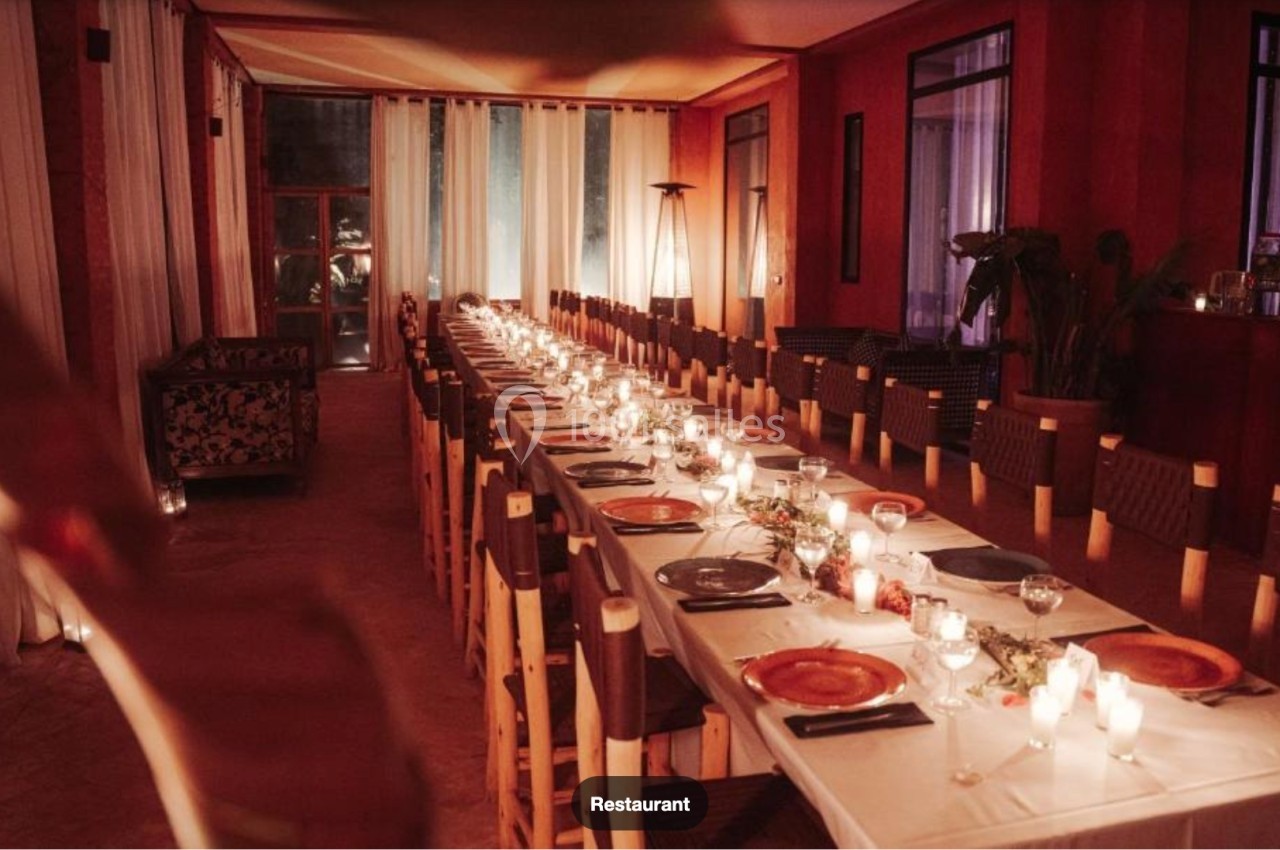 Salle de restaurant avec une longue table dressée, éclairée par des bougies et entourée de chaises en bois.