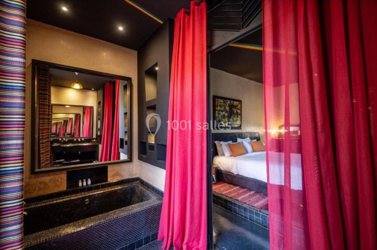 Chambre avec lit double, rideaux rouges, salle de bain attenante avec baignoire noire et miroir mural.