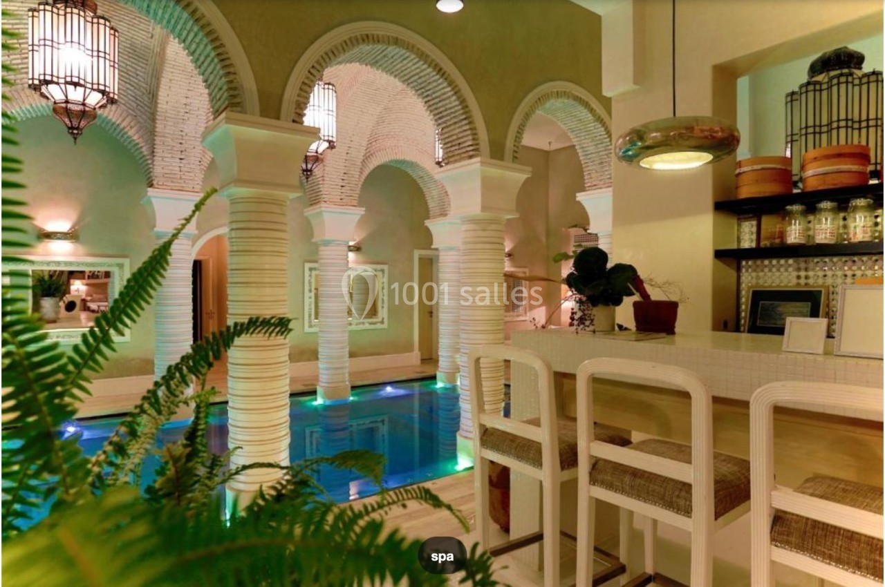 Espace intérieur avec piscine entourée de colonnes blanches, éclairage chaleureux et comptoir aménagé.