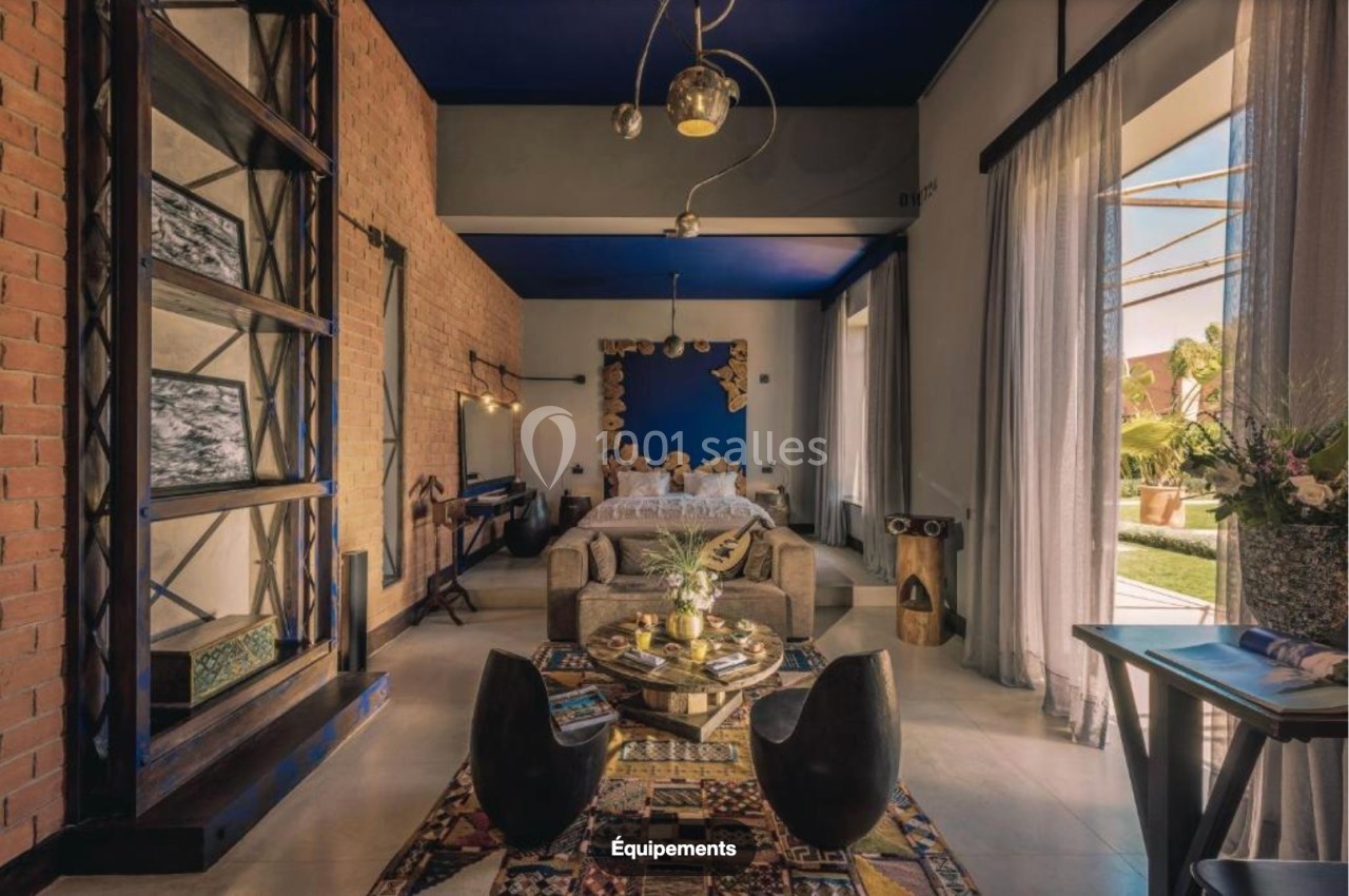 Intérieur d'une chambre lumineuse avec lit, coin salon, décoration éclectique et vue sur un jardin extérieur.