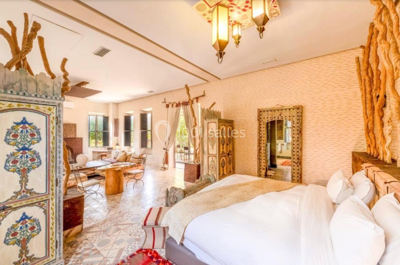 Chambre lumineuse avec lit double, décorations artisanales, mobilier en bois sculpté et grandes fenêtres donnant sur l…