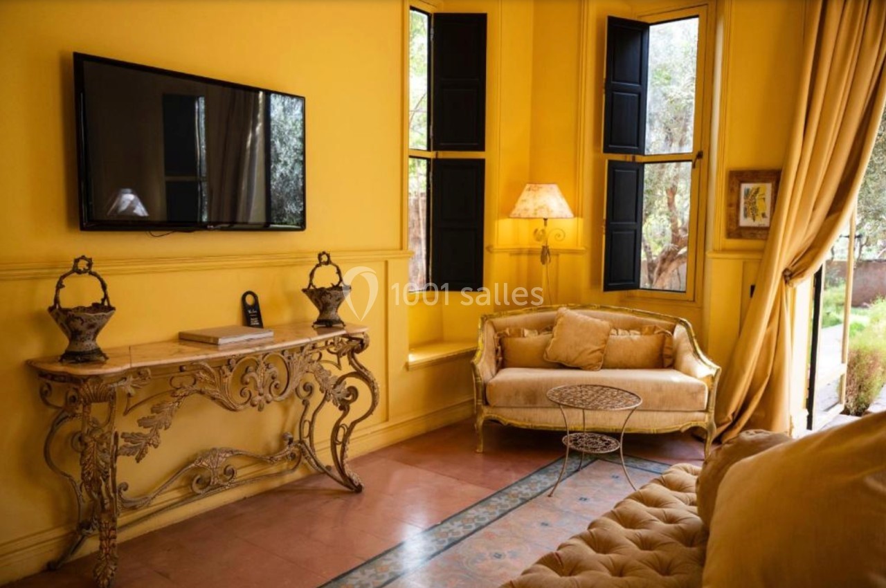 Salon lumineux avec murs jaunes, canapé beige, table basse, console décorative, téléviseur mural et grandes fenêtres.