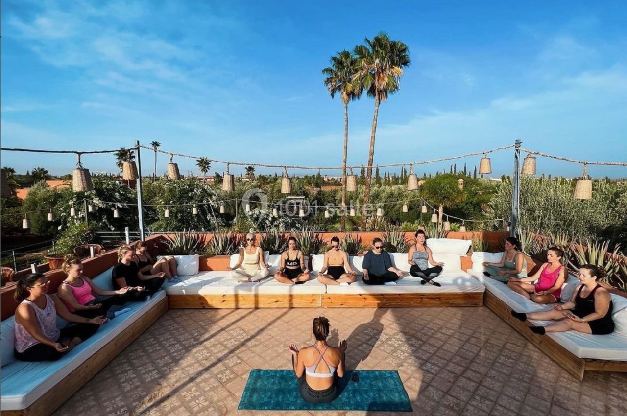 Un groupe de personnes assises en cercle sur une terrasse extérieure, participant à une séance de méditation.
