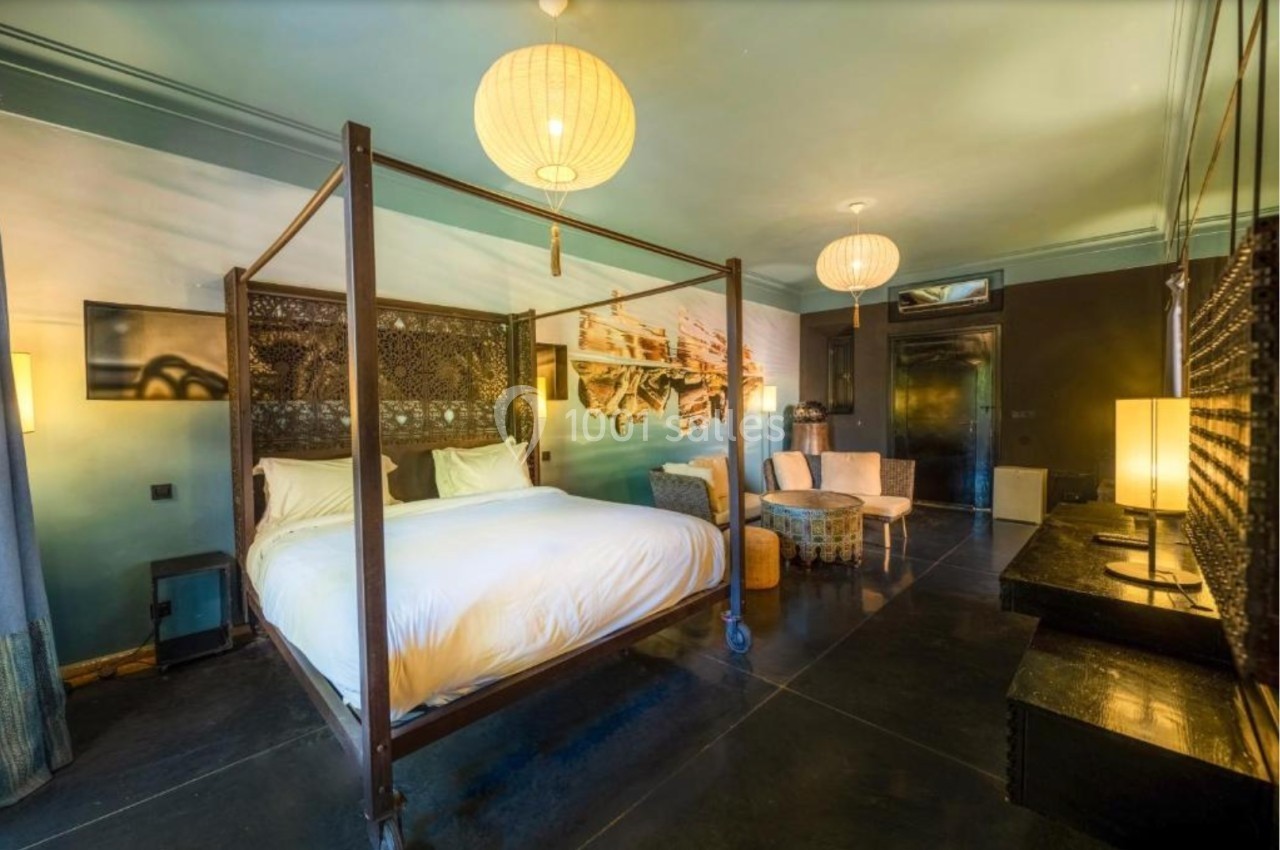 Chambre avec lit à baldaquin, décor mural artistique, fauteuils, lampes suspendues et éclairage tamisé.