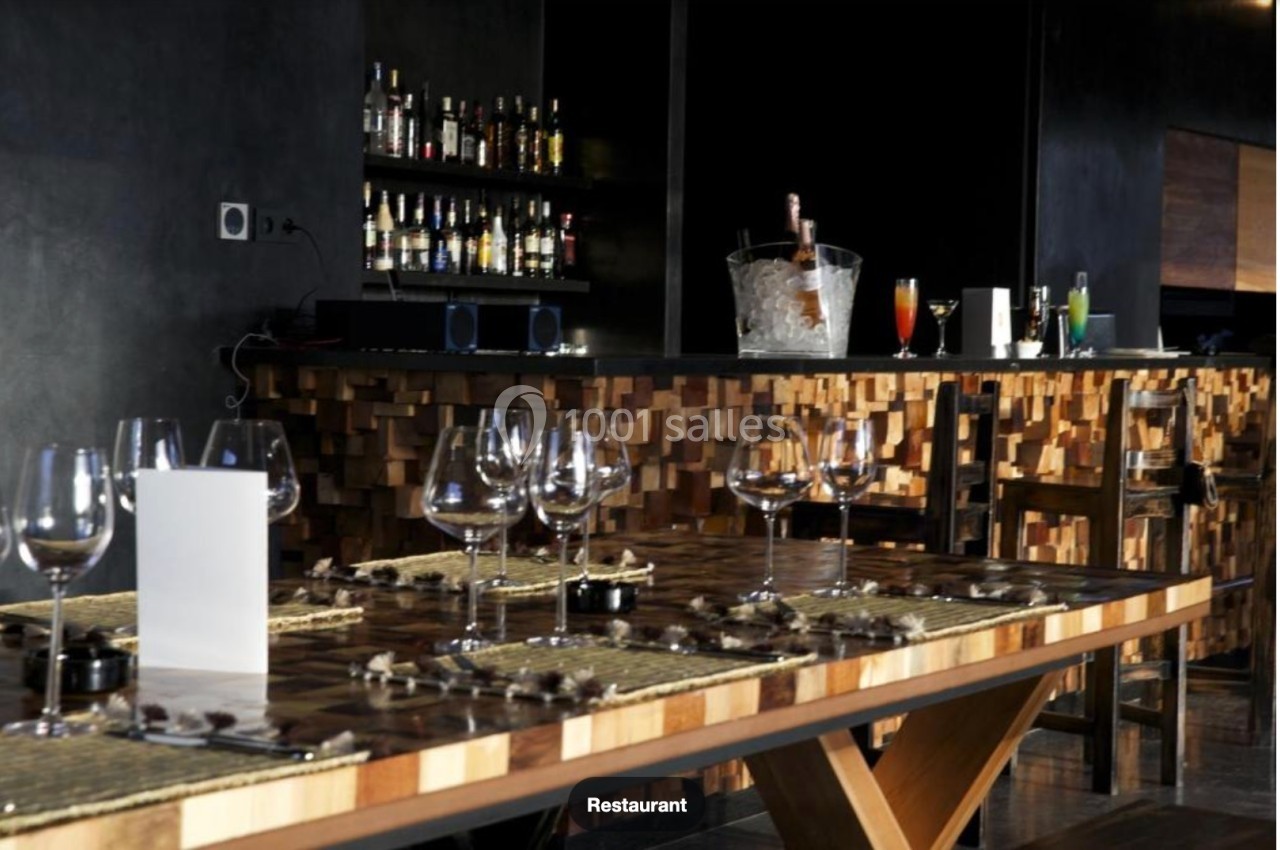 Intérieur d'un restaurant avec un bar en bois, des verres dressés sur une table et des bouteilles en arrière-plan.