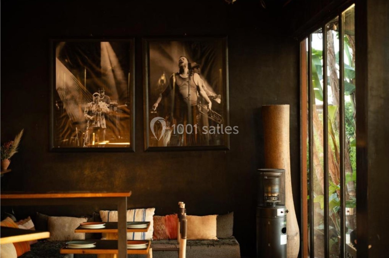 Espace intérieur chaleureux avec canapé, coussins, affiches de musiciens encadrées et grande baie vitrée donnant sur l…