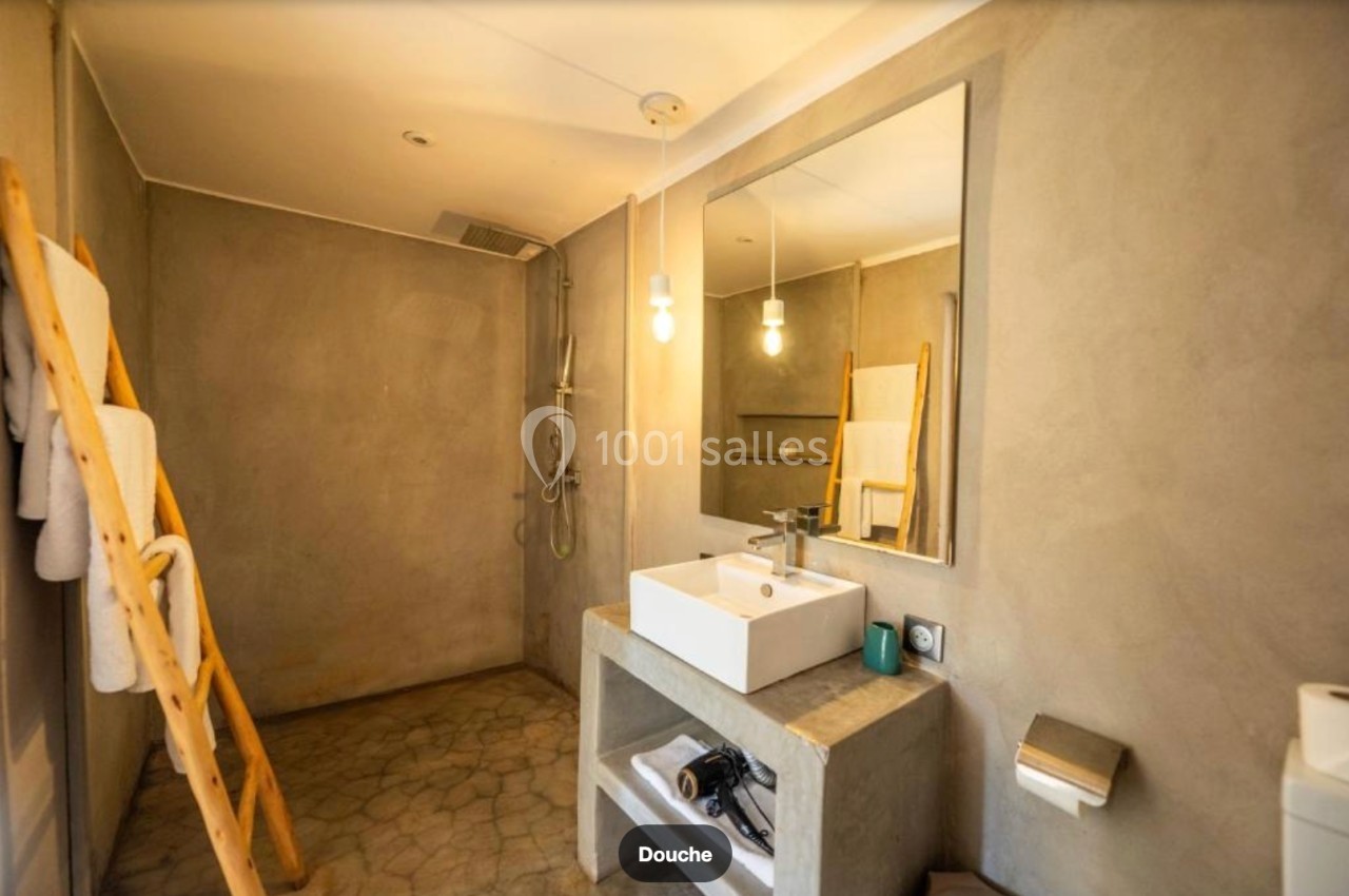 Salle de bain moderne avec murs en béton ciré, douche à l'italienne, lavabo blanc et échelle porte-serviettes en bois.