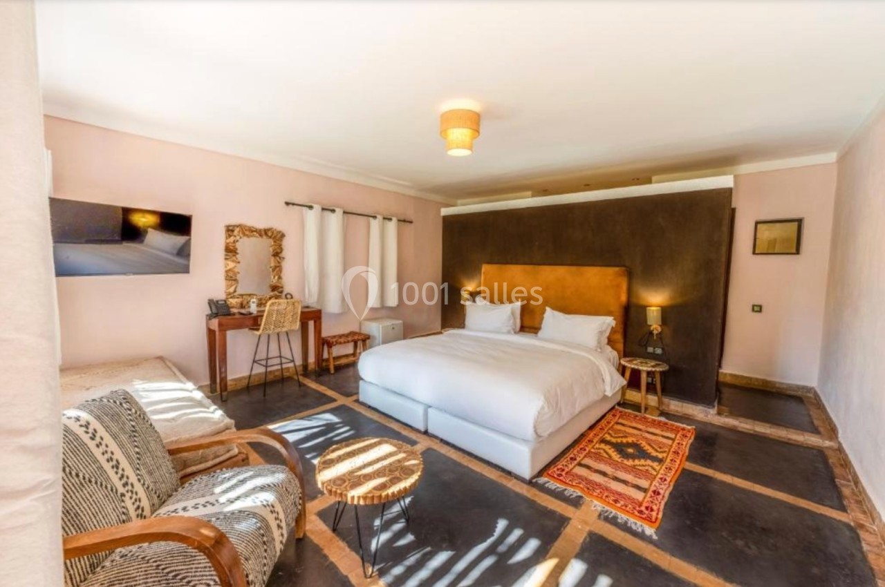 Chambre lumineuse avec lit double, bureau, fauteuils, tapis coloré et télévision, décorée dans un style chaleureux.