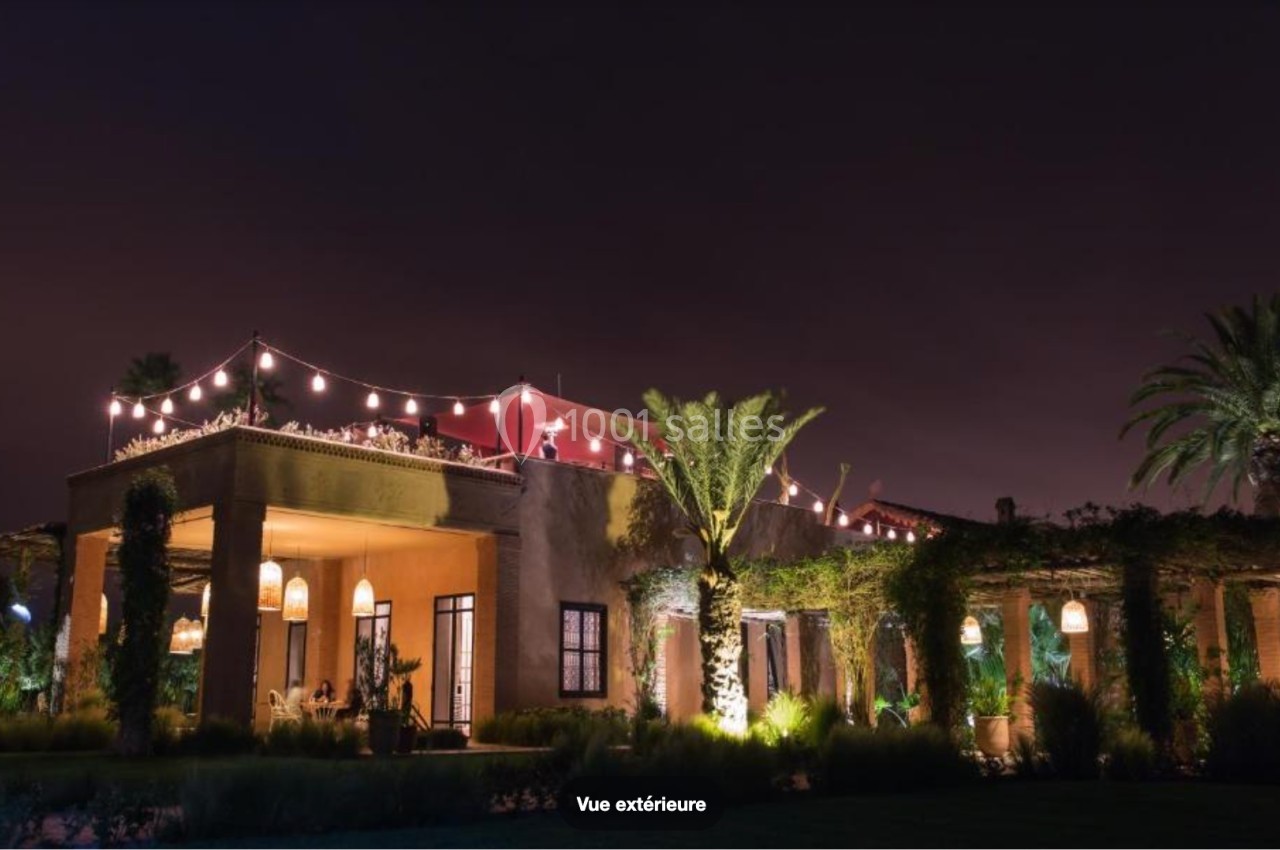 Façade d'un bâtiment éclairé la nuit, entouré de végétation et décoré de guirlandes lumineuses.