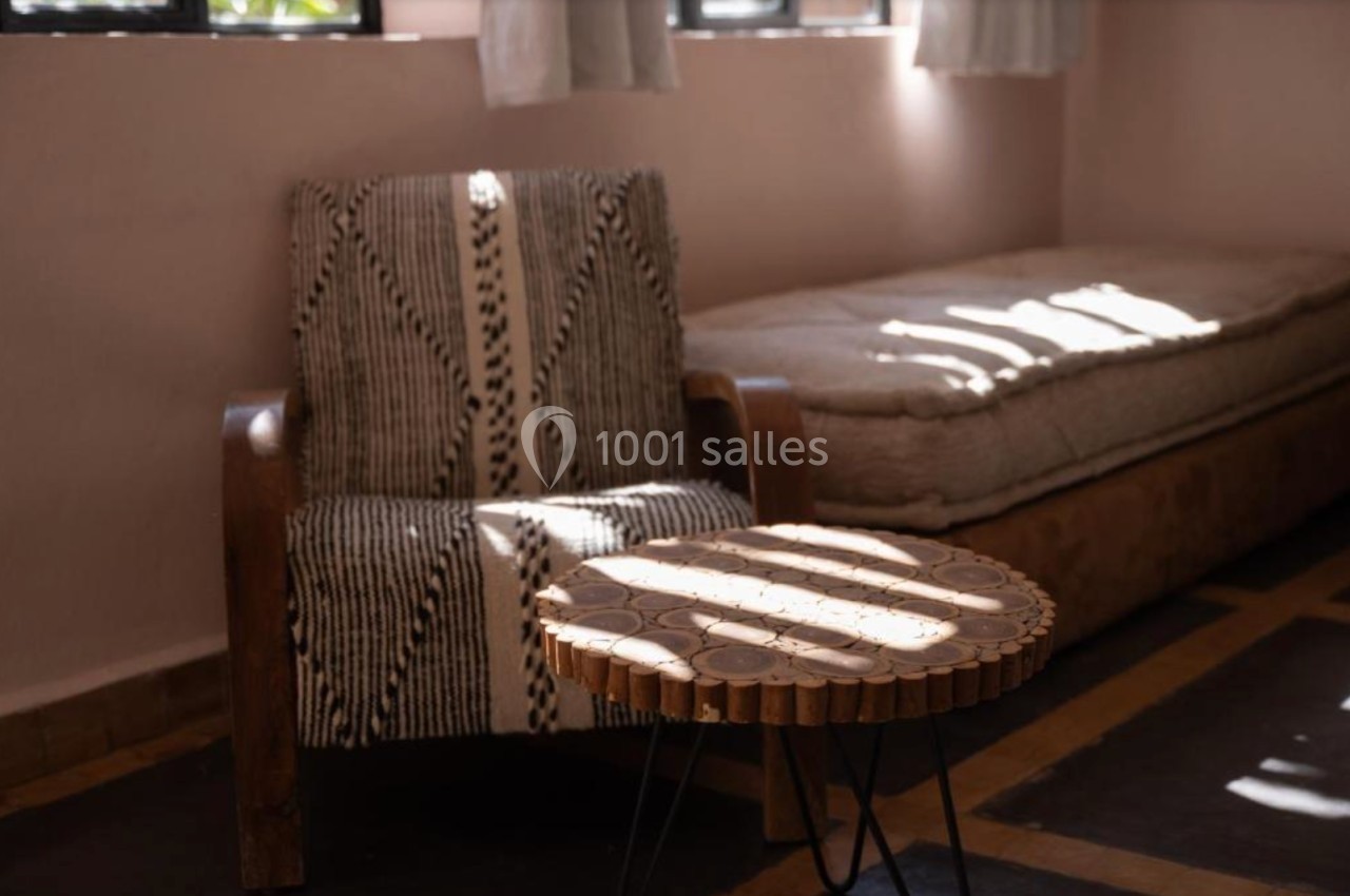 Fauteuil en bois avec tissu à motifs, table basse ronde en bois et banquette dans une pièce lumineuse.