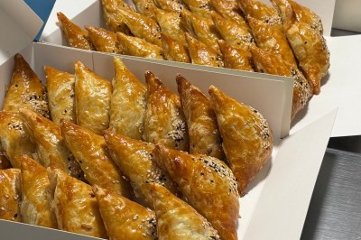 Un homme cuisine de grandes pièces de viande dans une marmite fumante en extérieur, portant un tablier et des gants.