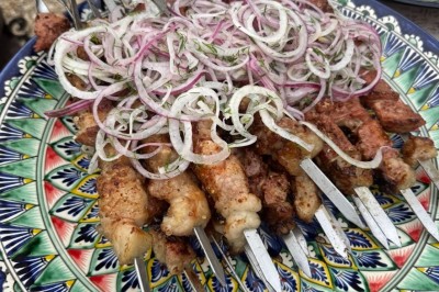 Un homme cuisine de grandes pièces de viande dans une marmite fumante en extérieur, portant un tablier et des gants.