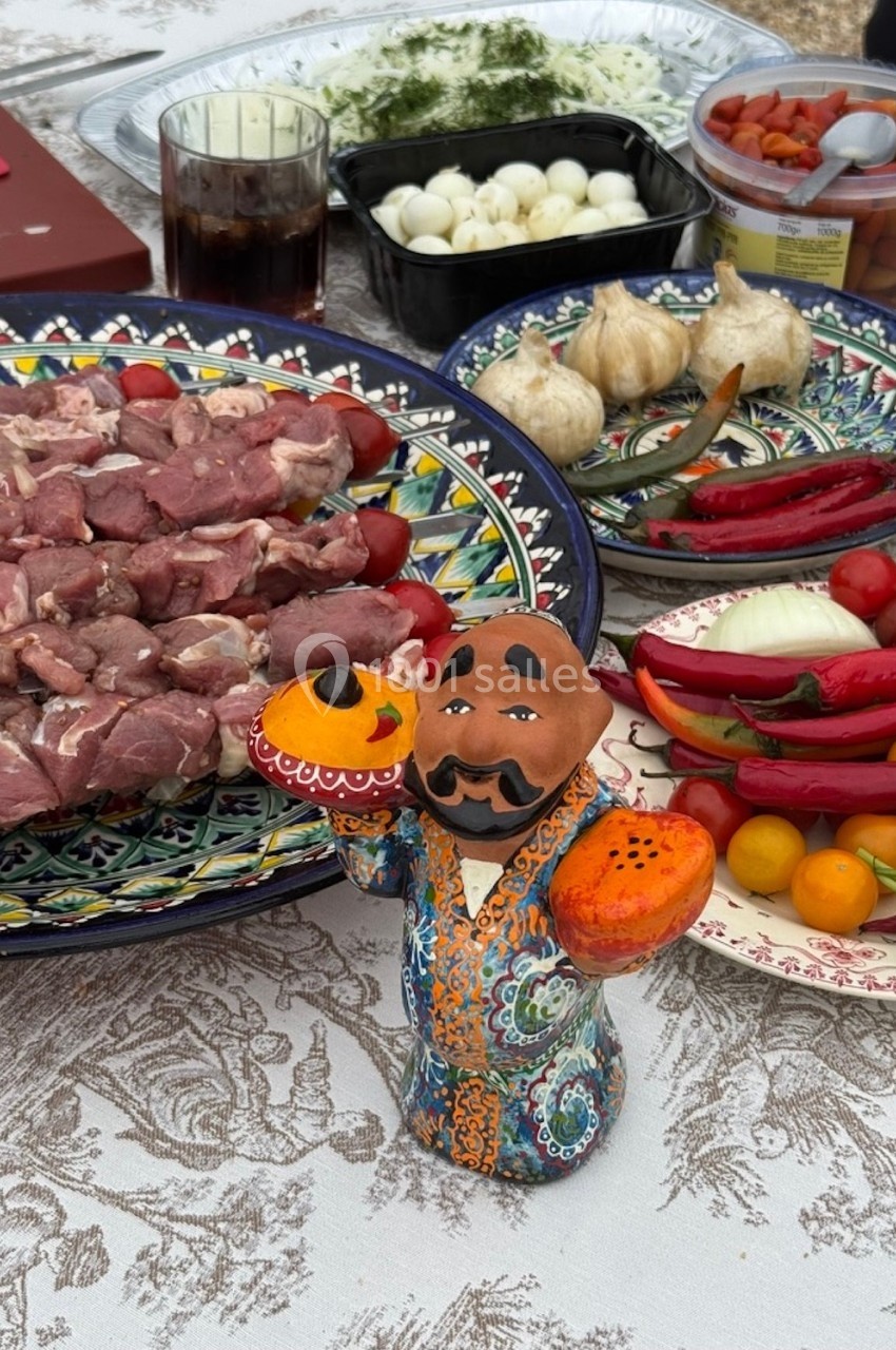 Assortiment de légumes, viandes crues et condiments sur une table décorée, avec une figurine colorée au premier plan.