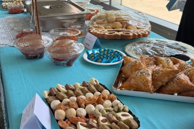 Un homme cuisine de grandes pièces de viande dans une marmite fumante en extérieur, portant un tablier et des gants.