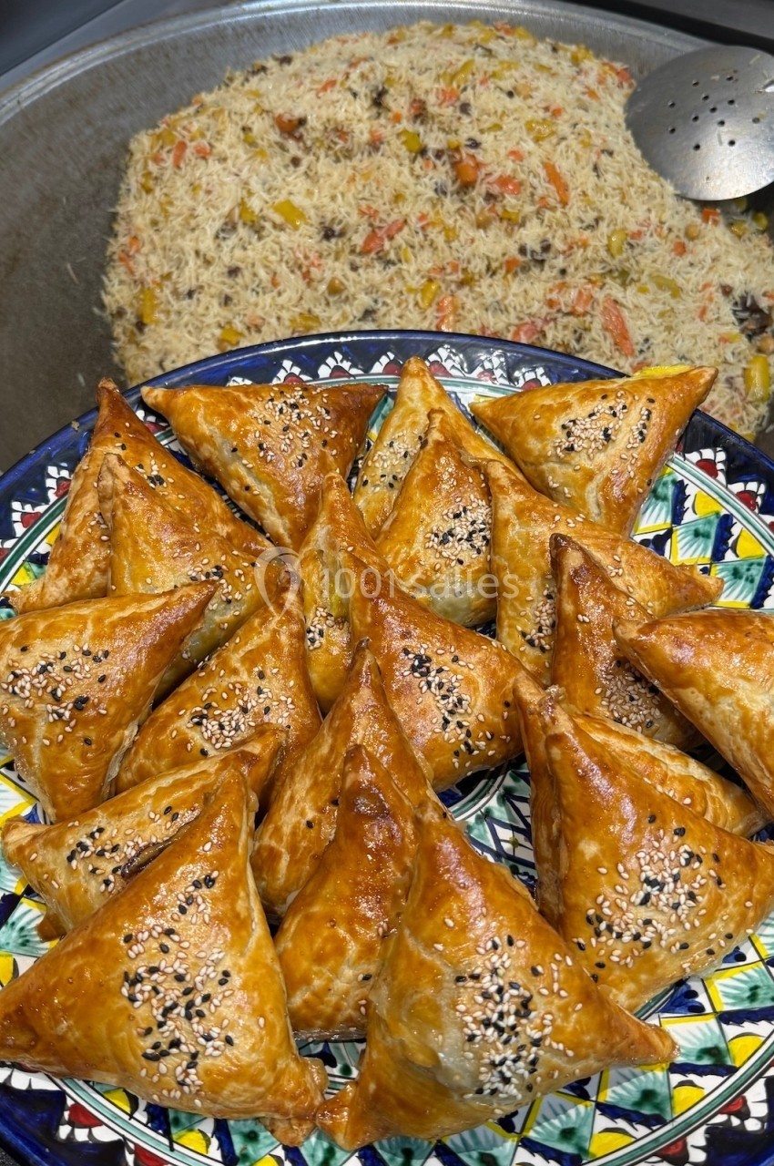 Assortiment de samoussas dorés garnis de graines de sésame, servis devant un plat de riz aux légumes et épices.