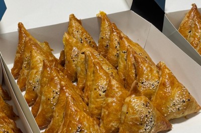 Un homme cuisine de grandes pièces de viande dans une marmite fumante en extérieur, portant un tablier et des gants.