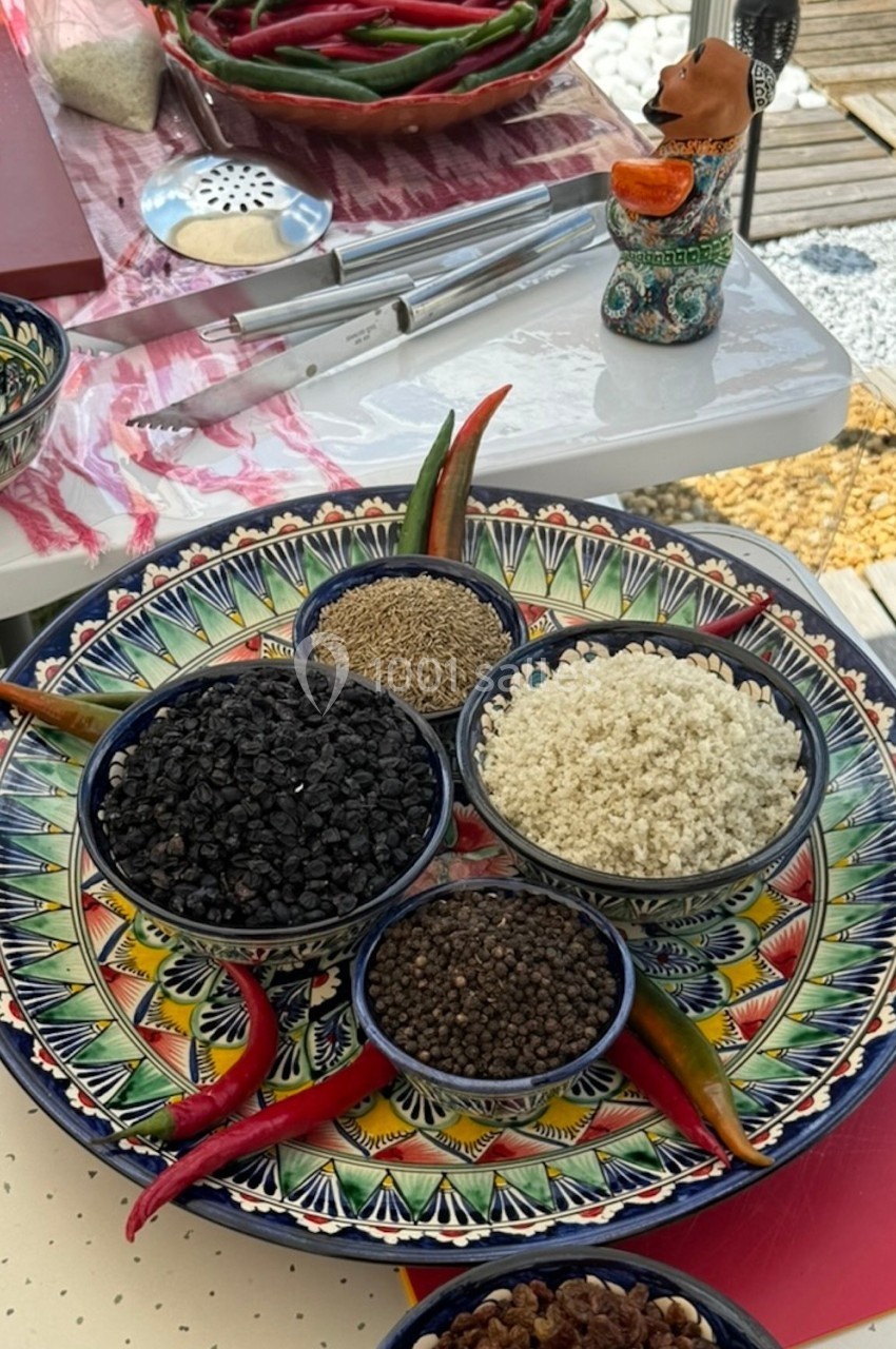 Assortiment d'épices en bols sur un plateau coloré, entouré de piments rouges et verts.