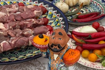 Assortiment d'ingrédients pour un repas, avec viande crue, légumes, herbes et une figurine décorative sur une nappe.