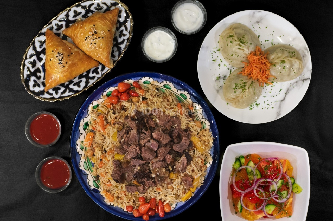 Assortiment de plats comprenant du riz avec viande, samoussas, raviolis vapeur et salade colorée, accompagnés de sauces.