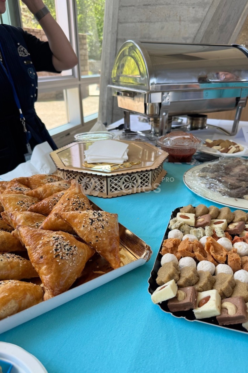 Table garnie de pâtisseries orientales, viennoiseries et desserts variés, avec un chauffe-plat en arrière-plan.