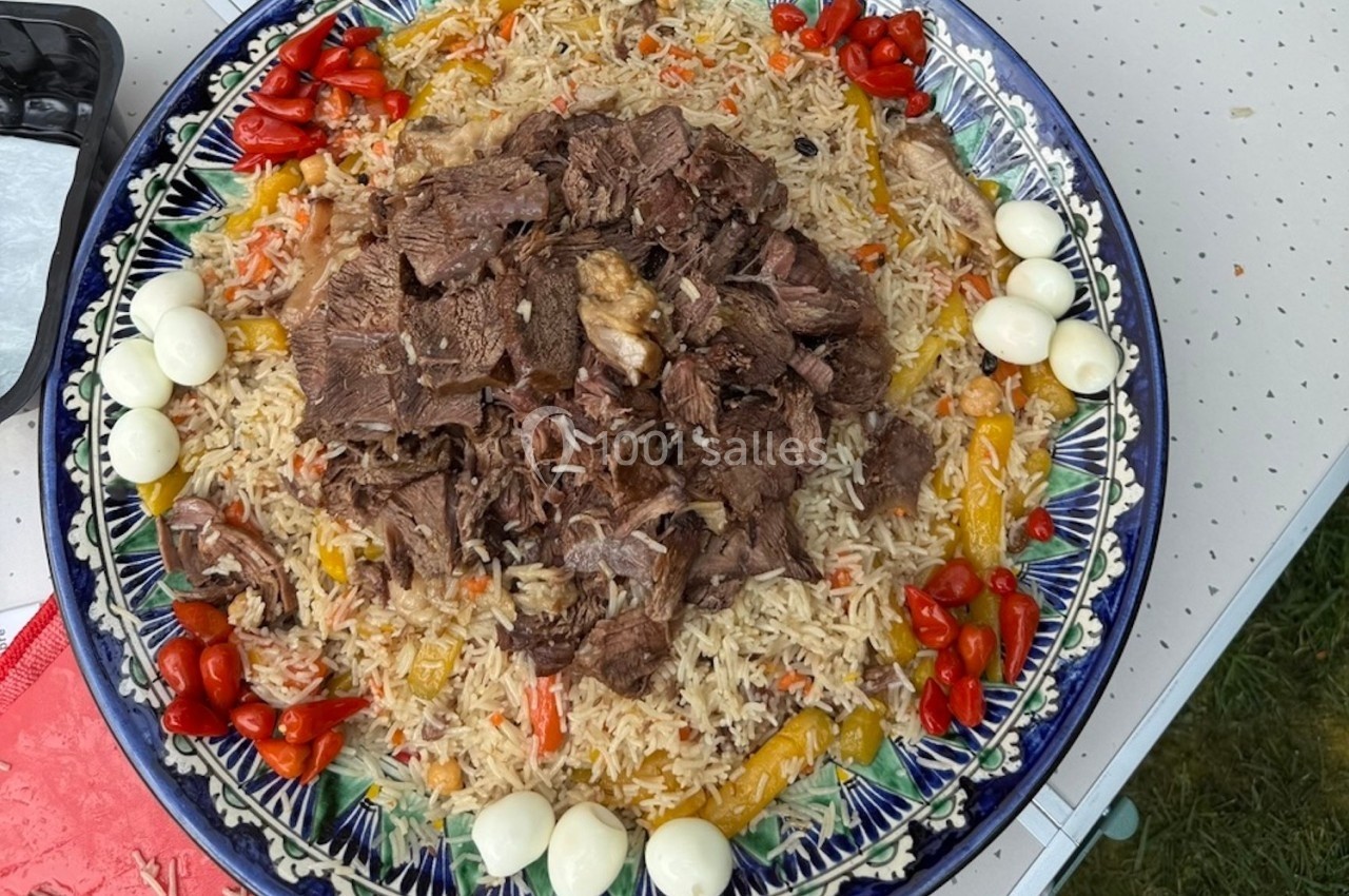 Plat de riz garni de morceaux de viande, légumes colorés et œufs de caille, présenté sur un grand plat décoré.