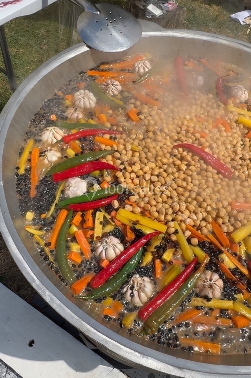 Grande poêle contenant pois chiches, carottes, poivrons, gousses d'ail et épices en cuisson à l'extérieur.
