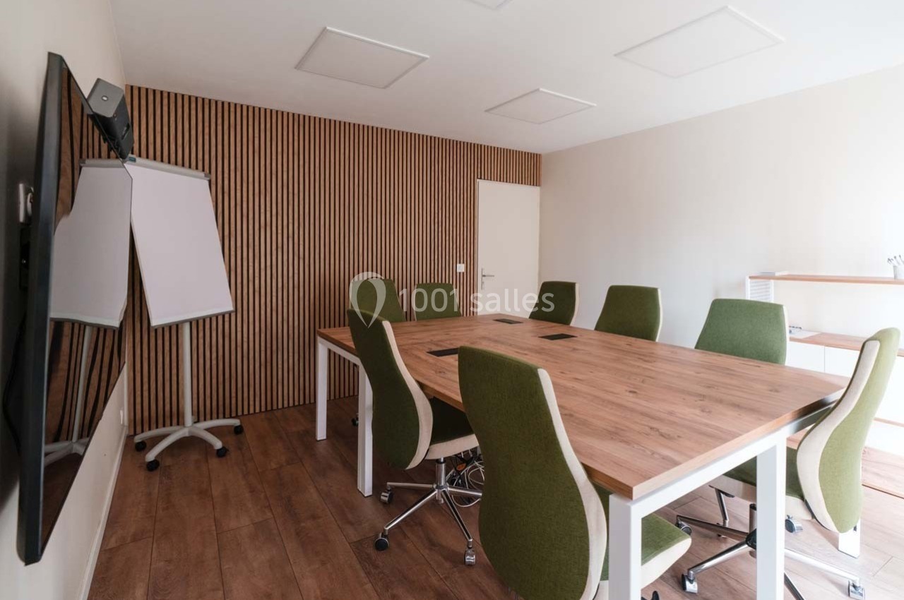 Salle de réunion lumineuse avec table en bois, chaises vertes, tableau blanc et mur en bois à l'arrière.