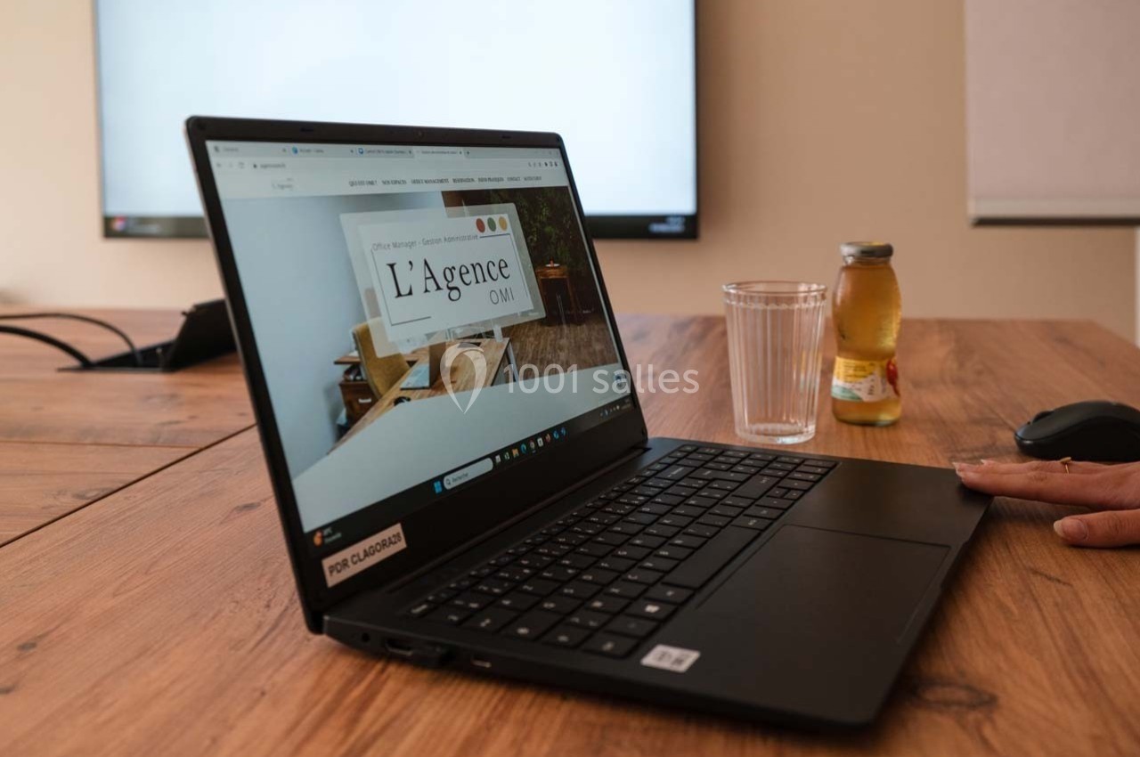 Ordinateur portable affichant une page web, posé sur une table en bois avec un verre d'eau et une bouteille de jus.
