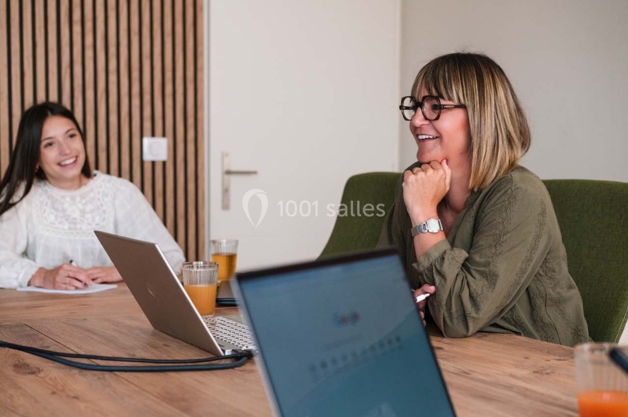Deux femmes discutent autour d'une table de réunion avec des ordinateurs portables et des verres de jus.
